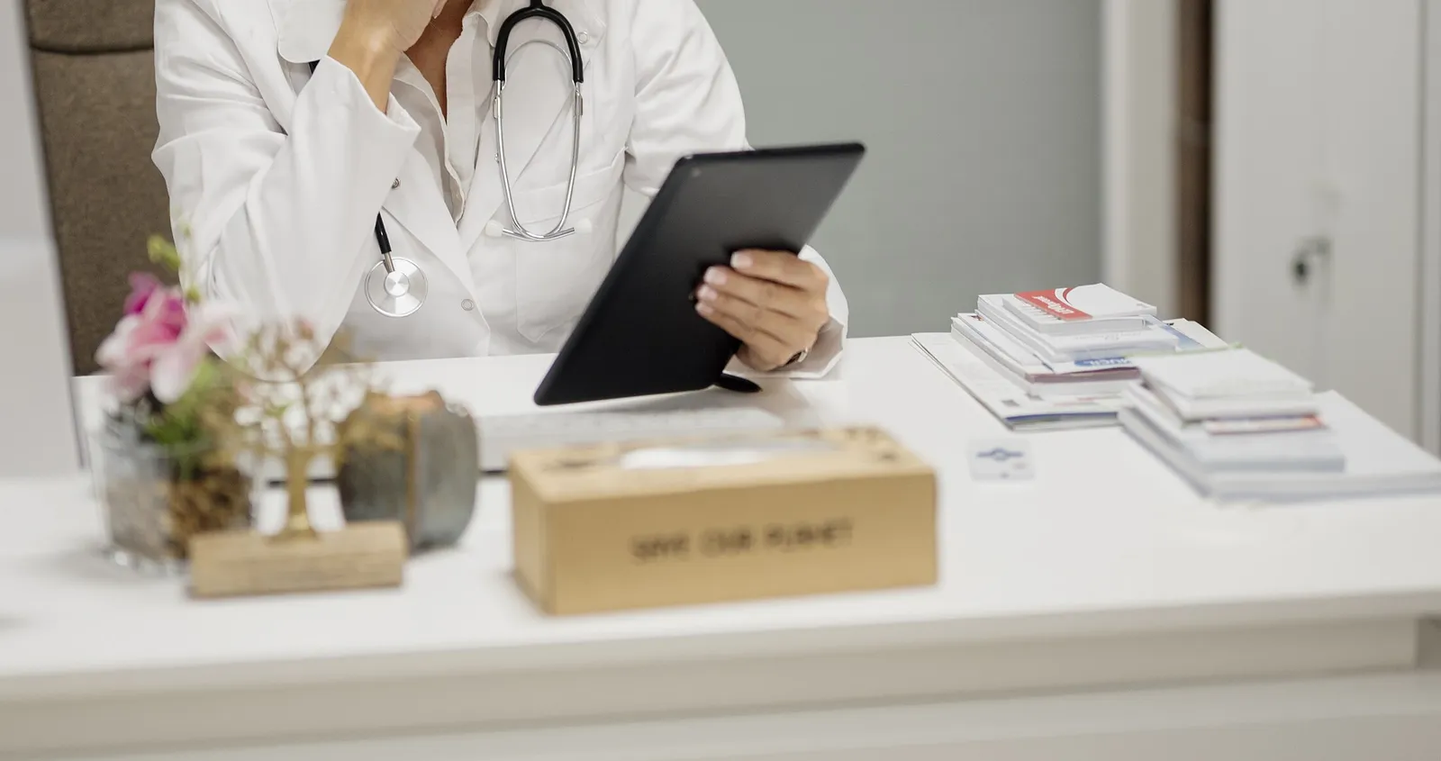 Doctor at a clinic desk reviewing records on a tablet