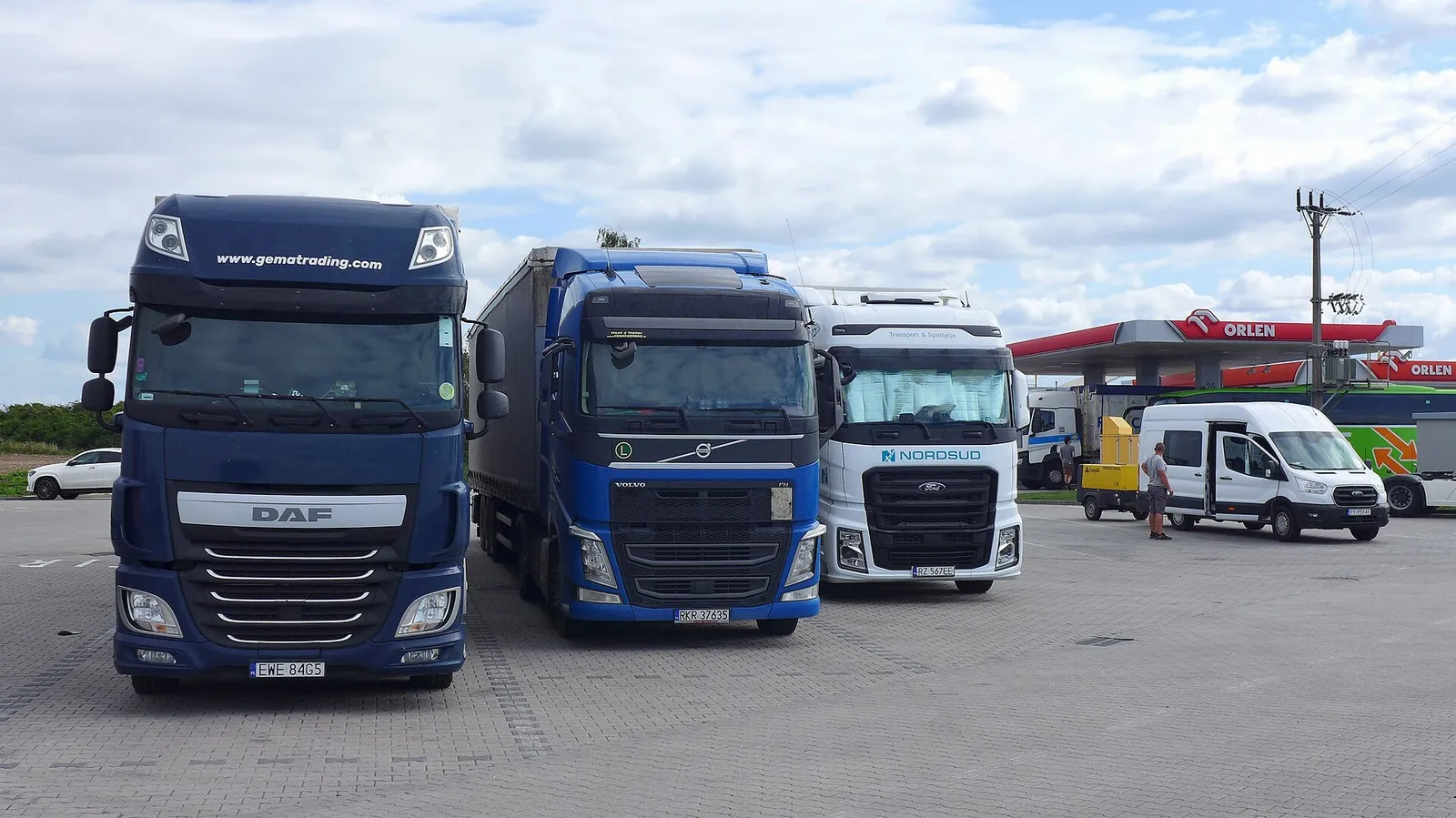 Three articulated freight trucks parked at a fuel station