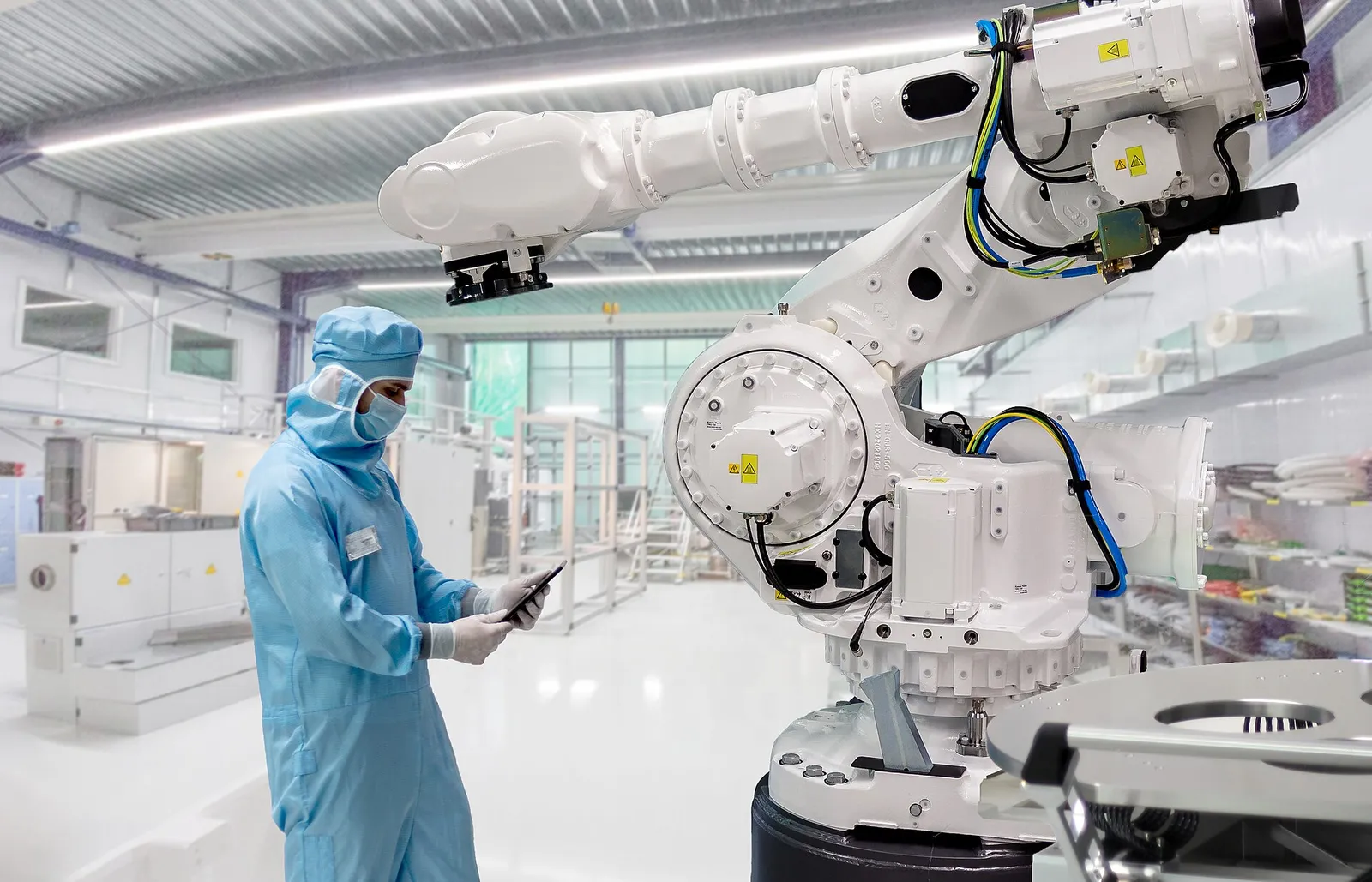 Engineer in cleanroom suit beside an industrial robot arm